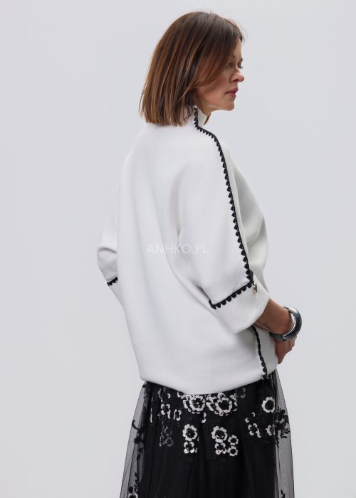Biała damska bluzka o luźnym kroju z półgolfem i rękawami 3/4, wykończona kontrastową czarną lamówką wzdłuż ramion, rękawów i boków oraz ozdobnymi guzikami przy mankietach