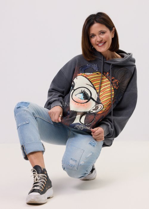 Grafitowa damska bluza z kapturem o luźnym kroju, z dużym artystycznym nadrukiem kobiecej twarzy z okularami i cekinowymi akcentami, noszona z jasnymi jeansami.