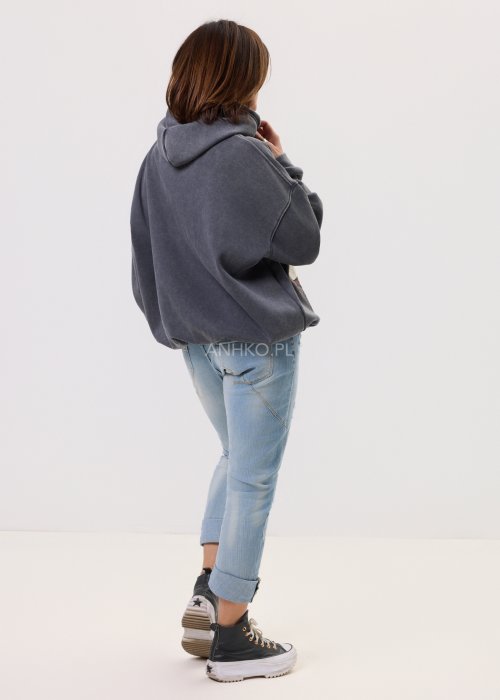 Grafitowa damska bluza z kapturem o luźnym kroju, z dużym artystycznym nadrukiem kobiecej twarzy z okularami i cekinowymi akcentami, noszona z jasnymi jeansami.