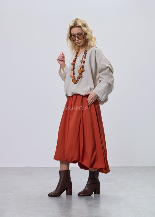 Beżowa bluzka damska oversize z dekoltem V i podwijanymi rękawami, zestawiona z ceglastą spódnicą w casualowej stylizacji.