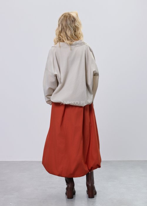 Beżowa bluzka damska oversize z dekoltem V i podwijanymi rękawami, zestawiona z ceglastą spódnicą w casualowej stylizacji.