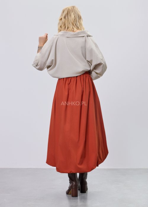 Beżowa bluzka damska oversize z dekoltem V i podwijanymi rękawami, zestawiona z ceglastą spódnicą w casualowej stylizacji.