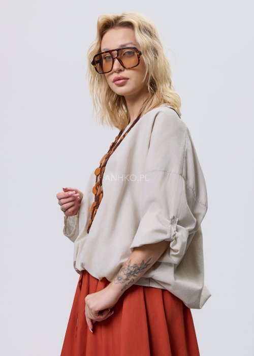 Beżowa bluzka damska oversize z dekoltem V i podwijanymi rękawami, zestawiona z ceglastą spódnicą w casualowej stylizacji.
