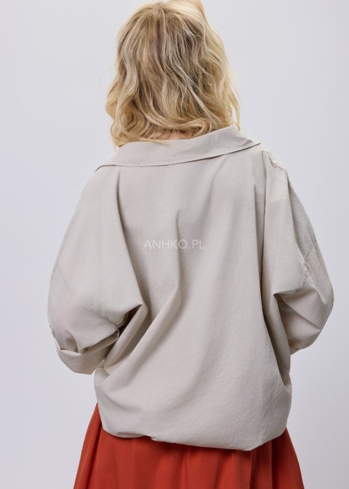 Beżowa bluzka damska oversize z dekoltem V i podwijanymi rękawami, zestawiona z ceglastą spódnicą w casualowej stylizacji.