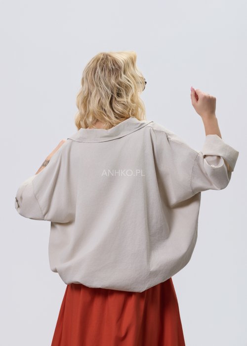 Beżowa bluzka damska oversize z dekoltem V i podwijanymi rękawami, zestawiona z ceglastą spódnicą w casualowej stylizacji.