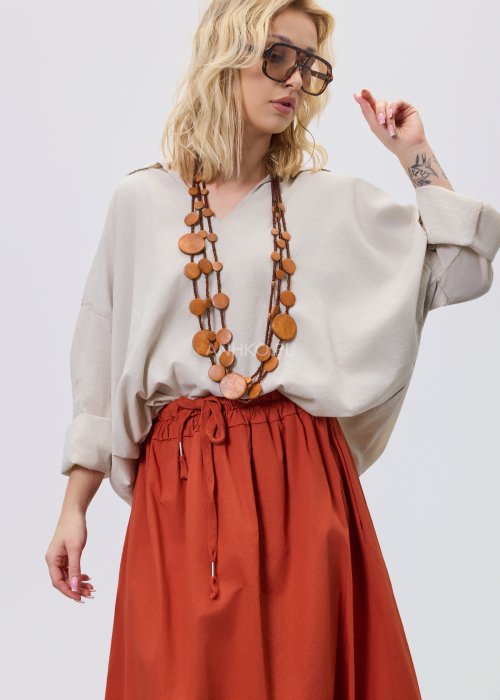 Beżowa bluzka damska oversize z dekoltem V i podwijanymi rękawami, zestawiona z ceglastą spódnicą w casualowej stylizacji.