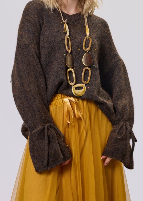 Brązowy sweter damski o luźnym kroju z ozdobnym wiązaniem na rękawach, zestawiony z musztardową spódnicą w stylu casual