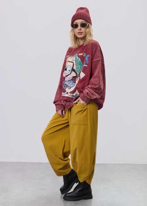 Bordowa bluza damska z efektem sprania i dużym, artystycznym nadrukiem, zestawiona z musztardowymi spodniami w stylu streetwear