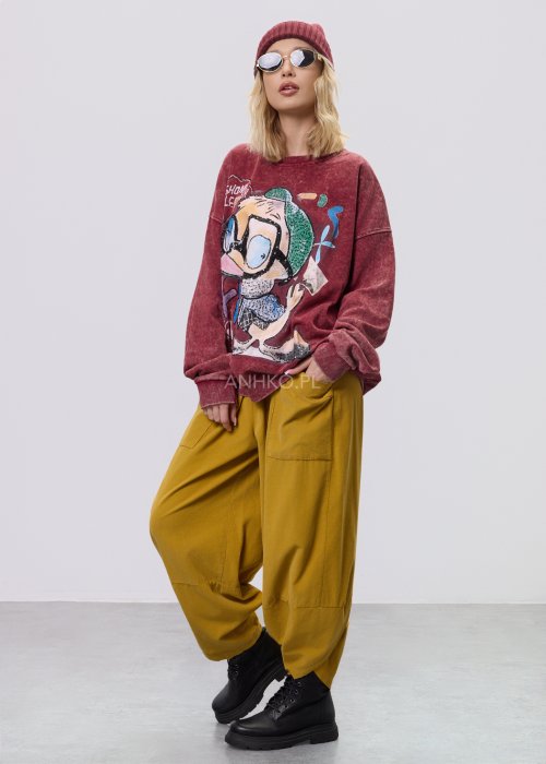 Bordowa bluza damska z efektem sprania i dużym, artystycznym nadrukiem, zestawiona z musztardowymi spodniami w stylu streetwear