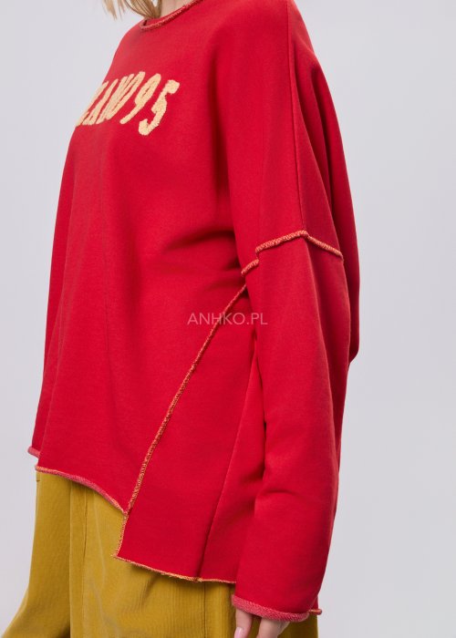 Czerwona bluza damska oversize z haftem „Milano 95” i kontrastowymi przeszyciami, zestawiona z musztardowymi spodniami w stylizacji miejskiej.