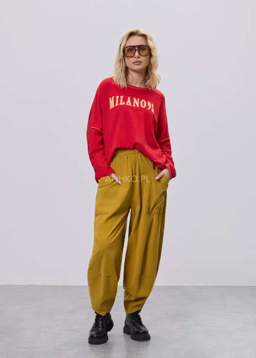 Czerwona bluza damska oversize z haftem „Milano 95” i kontrastowymi przeszyciami, zestawiona z musztardowymi spodniami w stylizacji miejskiej.