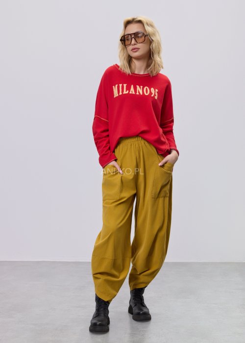Czerwona bluza damska oversize z haftem „Milano 95” i kontrastowymi przeszyciami, zestawiona z musztardowymi spodniami w stylizacji miejskiej.
