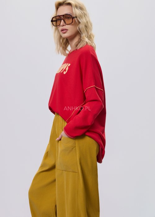 Czerwona bluza damska oversize z haftem „Milano 95” i kontrastowymi przeszyciami, zestawiona z musztardowymi spodniami w stylizacji miejskiej.