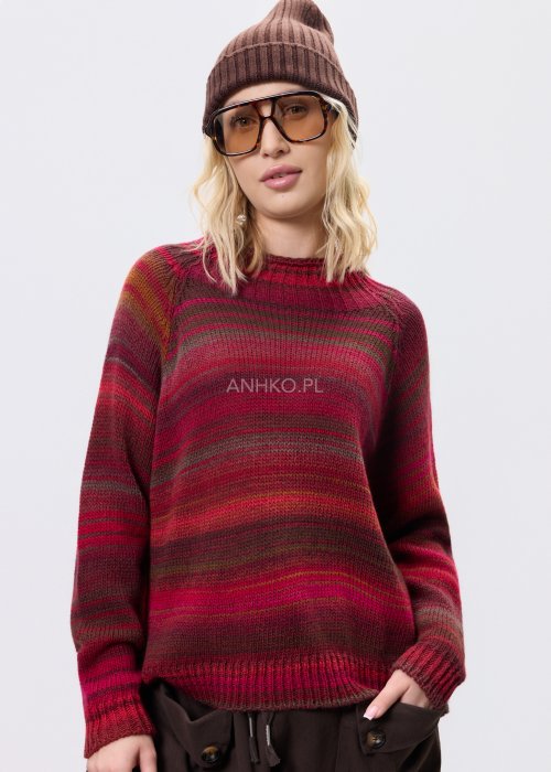 Bordowy sweter damski w wielobarwne paski w odcieniach ziemi, zestawiony z brązowymi spodniami w stylizacji casual na chłodniejsze dni.