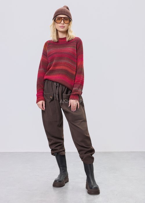 Bordowy sweter damski w wielobarwne paski w odcieniach ziemi, zestawiony z brązowymi spodniami w stylizacji casual na chłodniejsze dni.