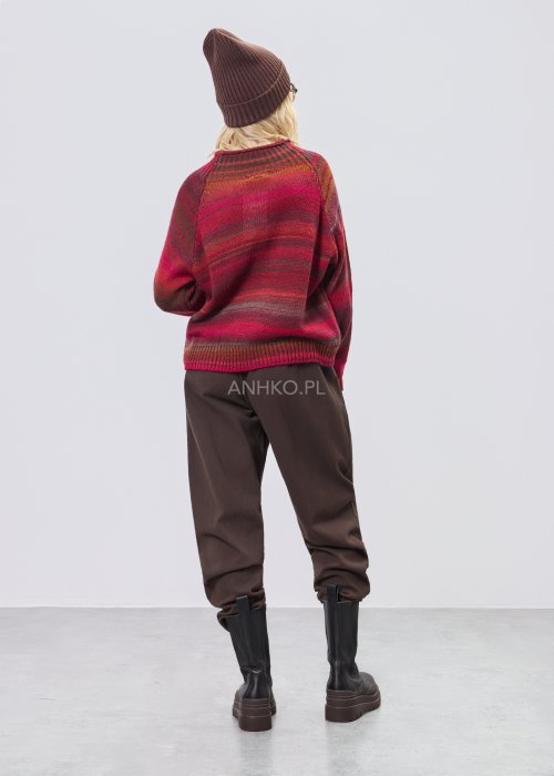 Bordowy sweter damski w wielobarwne paski w odcieniach ziemi, zestawiony z brązowymi spodniami w stylizacji casual na chłodniejsze dni.