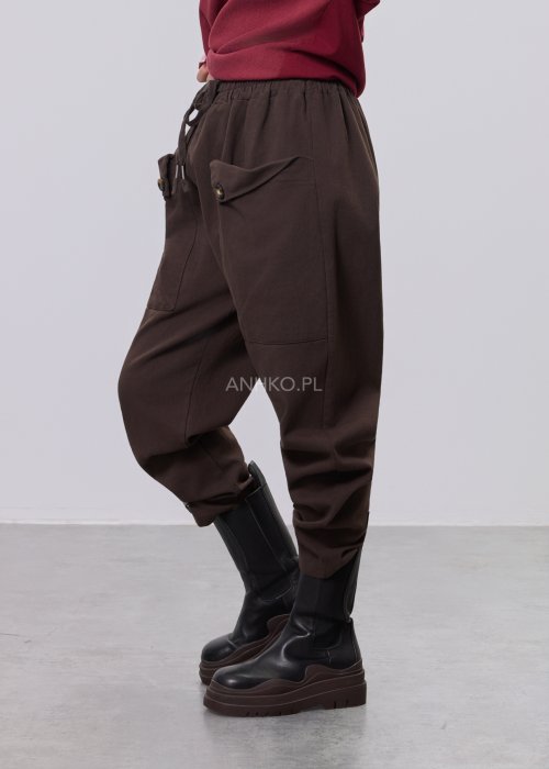 Brązowe spodnie sztruksowe o swobodnym kroju z elastyczną talią i kieszeniami zapinanymi na guziki, zestawione z botkami w stylizacji miejskiej.