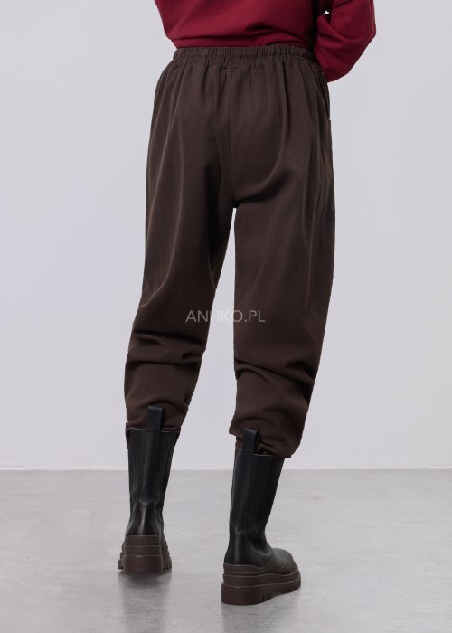 Brązowe spodnie sztruksowe o swobodnym kroju z elastyczną talią i kieszeniami zapinanymi na guziki, zestawione z botkami w stylizacji miejskiej.