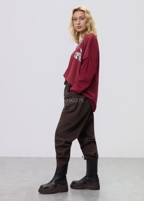 Brązowe spodnie sztruksowe o swobodnym kroju z elastyczną talią i kieszeniami zapinanymi na guziki, zestawione z botkami w stylizacji miejskiej.