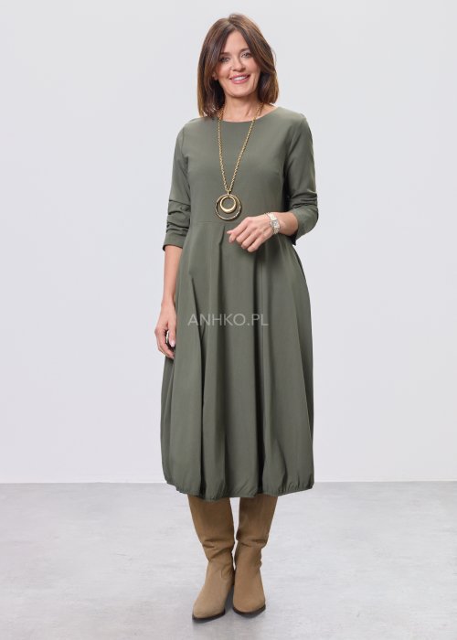 Ciemnozielona sukienka midi z długim rękawem, odcięciem w talii i kieszeniami, stylizowana z beżowymi kozakami.