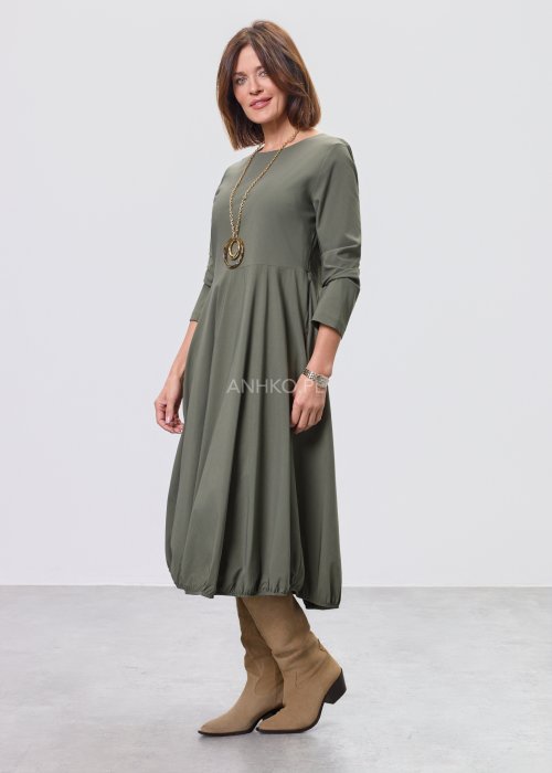 Ciemnozielona sukienka midi z długim rękawem, odcięciem w talii i kieszeniami, stylizowana z beżowymi kozakami.