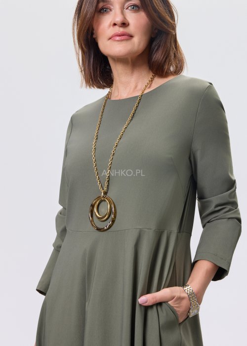 Ciemnozielona sukienka midi z długim rękawem, odcięciem w talii i kieszeniami, stylizowana z beżowymi kozakami.