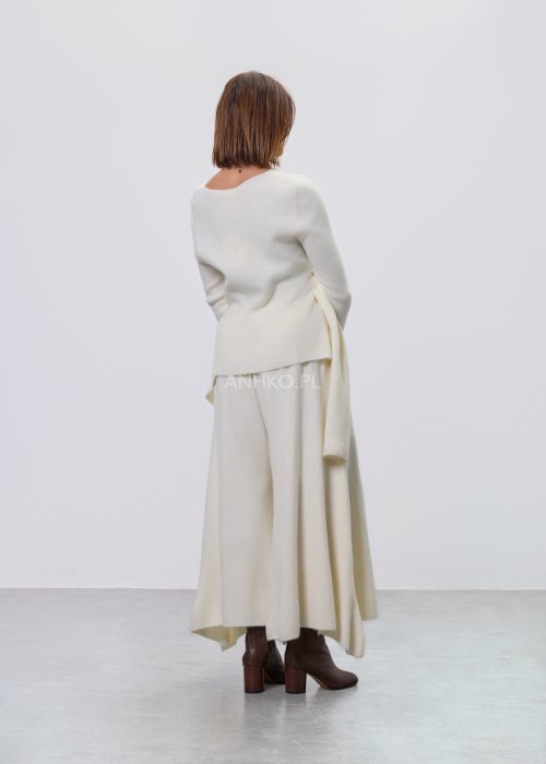 Śmietankowy komplet dzianinowy damski z asymetryczną tuniką i szerokimi spodniami, stylizowany z brązowymi botkami i torebką w minimalistycznym wnętrzu.