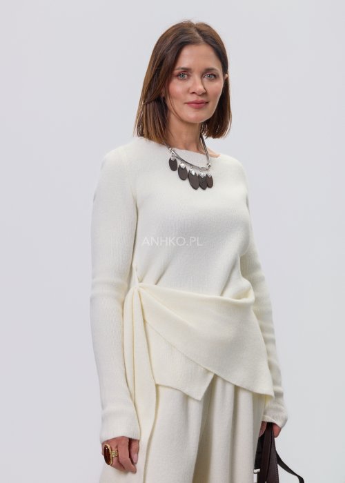 Śmietankowy komplet dzianinowy damski z asymetryczną tuniką i szerokimi spodniami, stylizowany z brązowymi botkami i torebką w minimalistycznym wnętrzu.