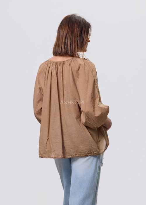 Camelowa bluzka damska z haftem przy dekolcie V i luźnym krojem, zestawiona z jasnymi jeansami w stylizacji casual.