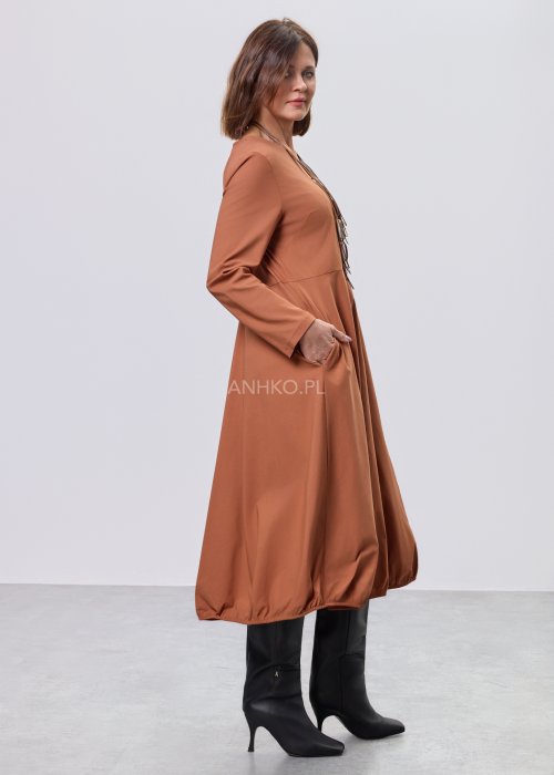 Karmelowa sukienka midi z długim rękawem, odcięciem w talii i kieszeniami, stylizowana z czarnymi kozakami.