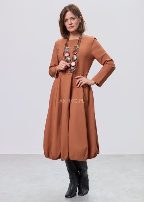 Karmelowa sukienka midi z długim rękawem, odcięciem w talii i kieszeniami, stylizowana z czarnymi kozakami.