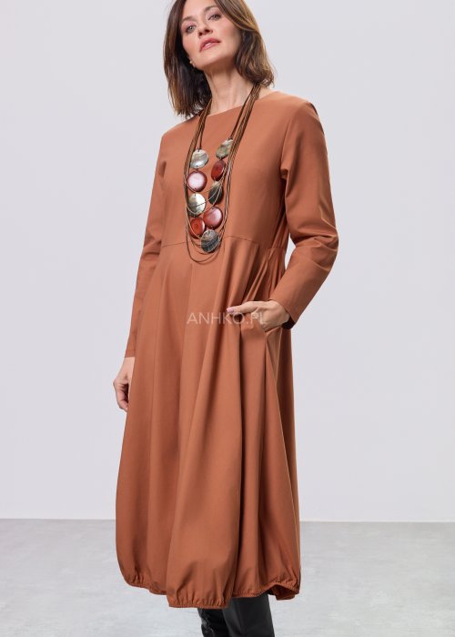 Karmelowa sukienka midi z długim rękawem, odcięciem w talii i kieszeniami, stylizowana z czarnymi kozakami.