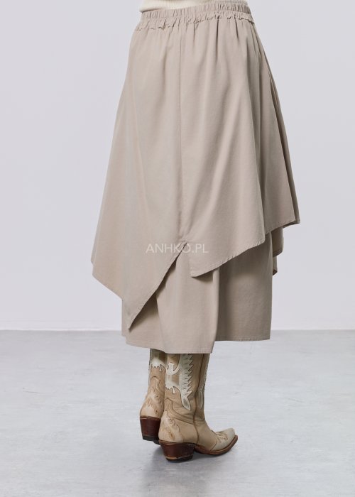 Beżowa spódnica midi o asymetrycznym, warstwowym kroju z elastycznym pasem i kieszeniami, stylizowana z kowbojkami.