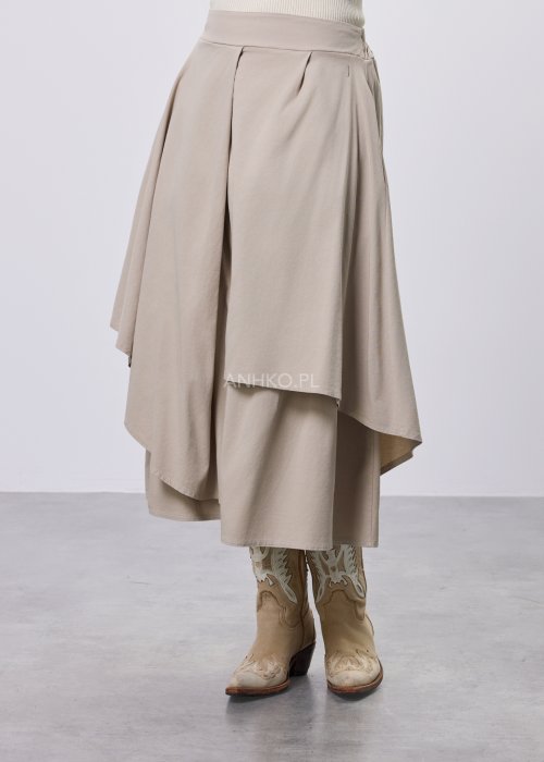 Beżowa spódnica midi o asymetrycznym, warstwowym kroju z elastycznym pasem i kieszeniami, stylizowana z kowbojkami.