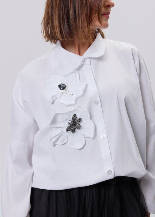 Biała koszula damska z przestrzenną aplikacją 3D na przodzie, luźny fason z długim rękawem, stylizacja z czarną spódnicą tiulową.