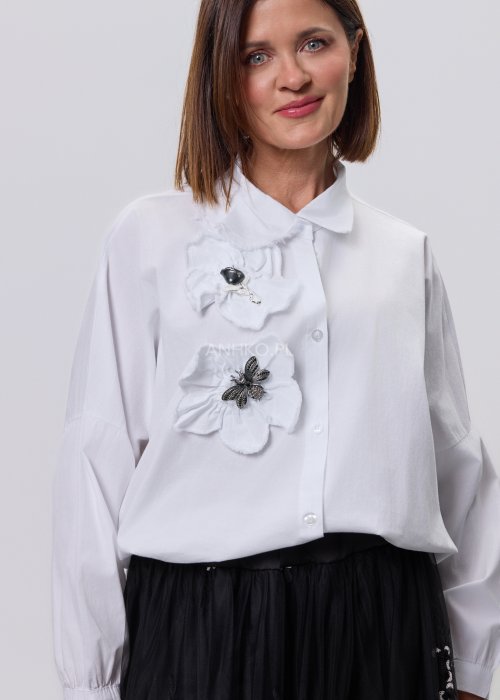 Biała koszula damska z przestrzenną aplikacją 3D na przodzie, luźny fason z długim rękawem, stylizacja z czarną spódnicą tiulową.