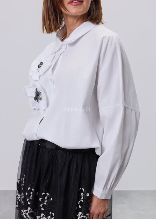 Biała koszula damska z przestrzenną aplikacją 3D na przodzie, luźny fason z długim rękawem, stylizacja z czarną spódnicą tiulową.