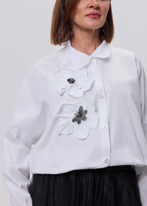 Biała koszula damska z przestrzenną aplikacją 3D na przodzie, luźny fason z długim rękawem, stylizacja z czarną spódnicą tiulową.