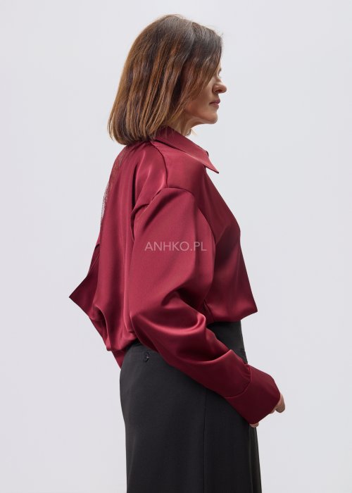 Bordowa koszula damska z satynowym wykończeniem i koronkowym tyłem, zestawiona z czarną spódnicą o rozkloszowanym kroju.
