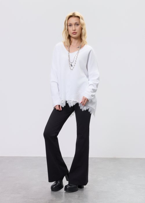 Biała bluzka damska o luźnym kroju z dekoltem V i koronkowym wykończeniem u dołu, zestawiona z czarnymi spodniami w stylizacji casual.