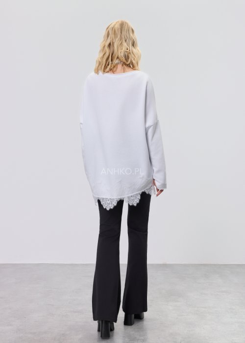 Biała bluzka damska o luźnym kroju z dekoltem V i koronkowym wykończeniem u dołu, zestawiona z czarnymi spodniami w stylizacji casual.