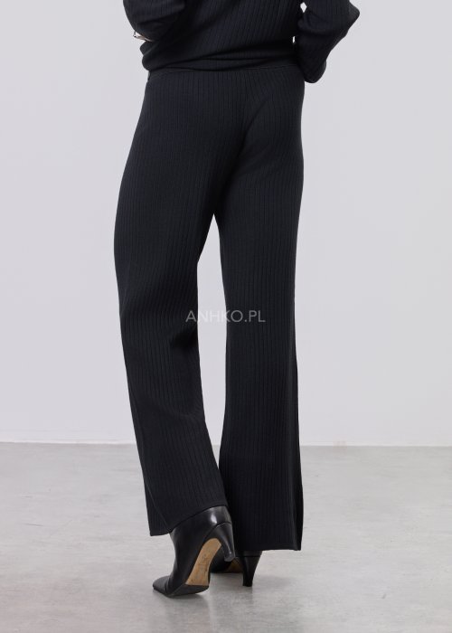 Czarny komplet dzianinowy z bluzką z dekoltem w serek i prostymi spodniami, stylizowany z czarnymi botkami.