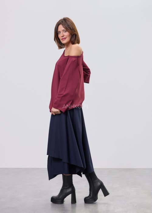Bordowa bluza damska oversize z raglanowymi rękawami i asymetrycznym dekoltem, stylizowana z granatową spódnicą midi i czarnymi botkami.