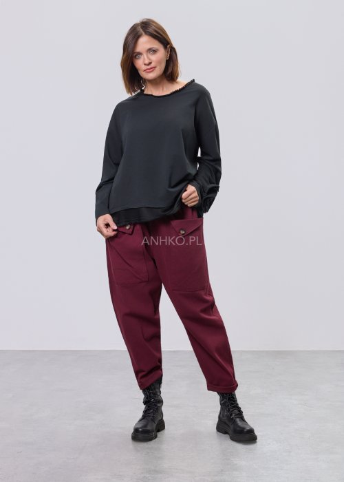 Czarna luźna bluzka z długim rękawem i surowym wykończeniem dekoltu, zestawiona z bordowymi spodniami.