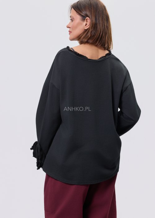 Czarna luźna bluzka z długim rękawem i surowym wykończeniem dekoltu, zestawiona z bordowymi spodniami.
