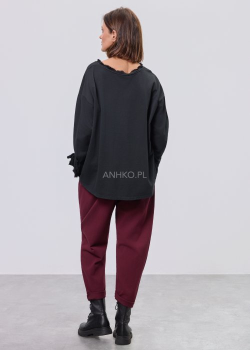 Czarna luźna bluzka z długim rękawem i surowym wykończeniem dekoltu, zestawiona z bordowymi spodniami.