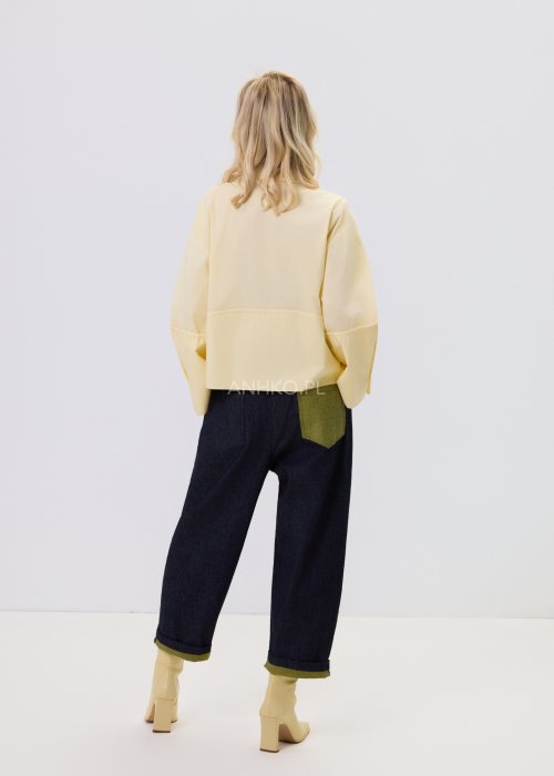 Jasnożółta koszula damska Velin Soft o luźnym kroju z klasycznym kołnierzykiem, dłuższym tyłem i poszerzanymi rękawami, stylizowana z ciemnymi spodniami.