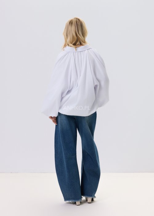 Biała koszula damska oversize z bufiastymi rękawami i elastycznym dołem, zestawiona z jeansami w nowoczesnej, minimalistycznej stylizacji.