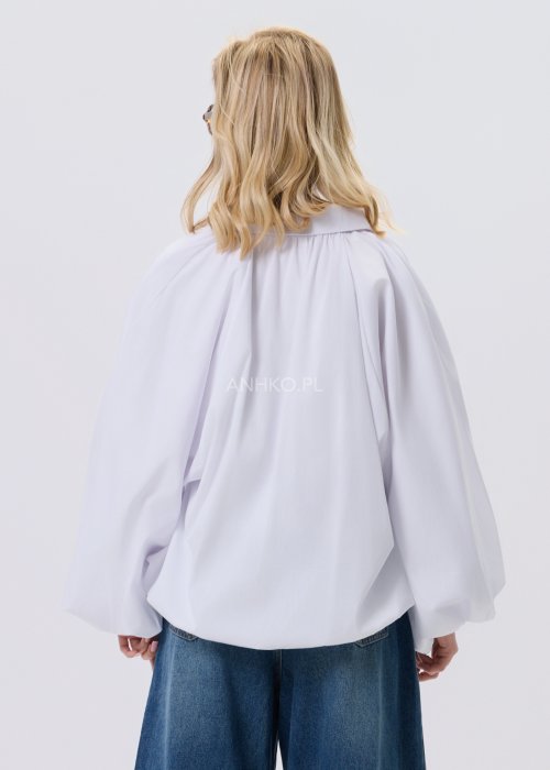 Biała koszula damska oversize z bufiastymi rękawami i elastycznym dołem, zestawiona z jeansami w nowoczesnej, minimalistycznej stylizacji.