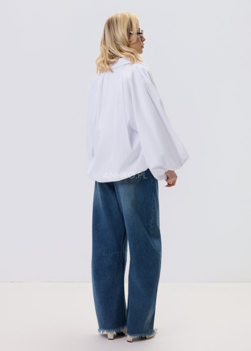 Biała koszula damska oversize z bufiastymi rękawami i elastycznym dołem, zestawiona z jeansami w nowoczesnej, minimalistycznej stylizacji.